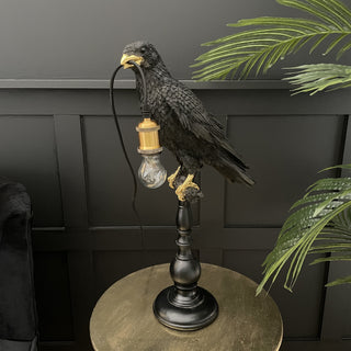 Black crow on a stick table lamp with a bulb in it's mouth